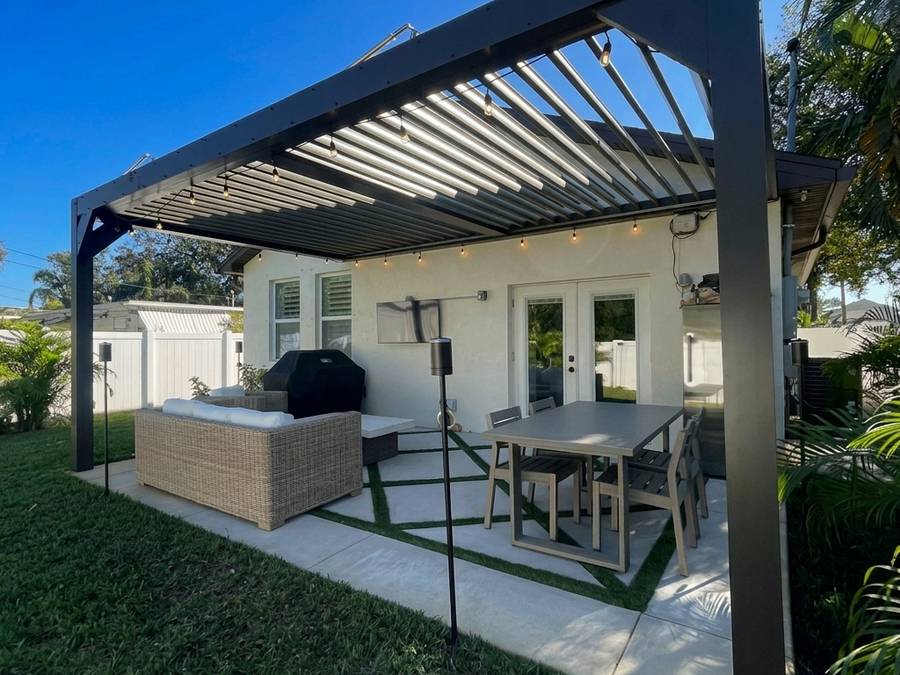 Matte black louvered pergola attached over a back patio slab with a dining table beneath