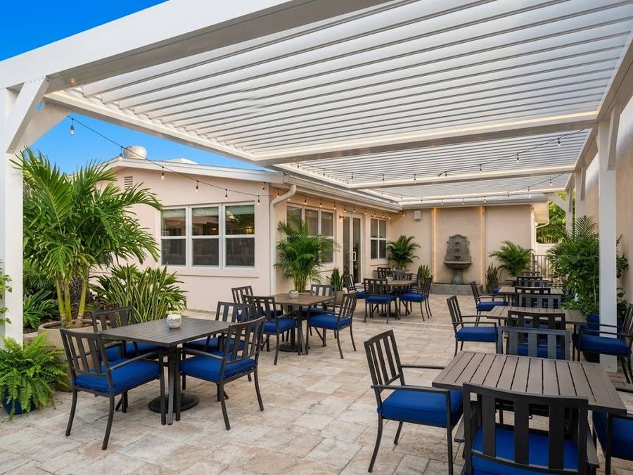 Three bays of white louvered pergola over a paved restaurant courtyard