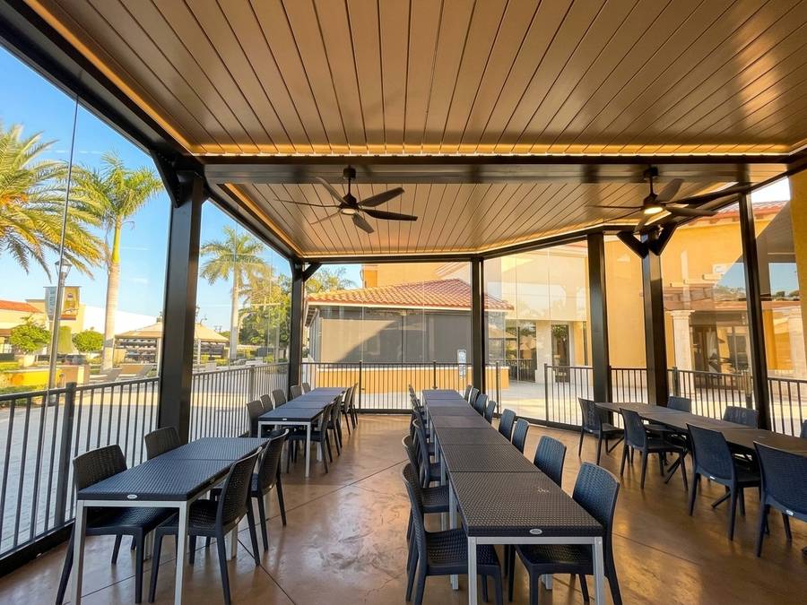 Long run of matte black louvered pergola with ceiling fans over waterfront restaurant seating