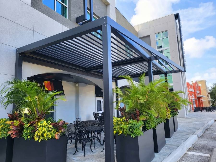 Two bays of matte black louvered pergola over sidewalk dining tables outside a storefront